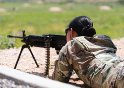 Female military personnel practice shooting at outdoor range.