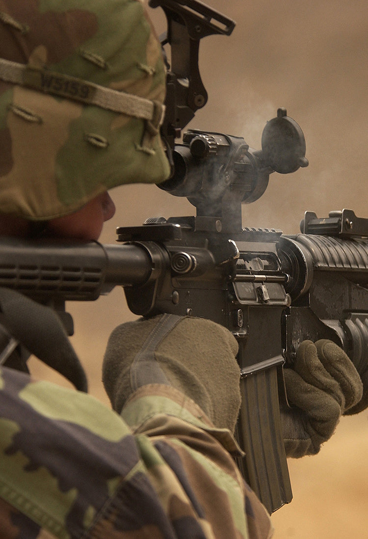 A person in combat gear firing a rifle.